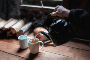 A hand, holding a kettle, pouring water into a teacup.