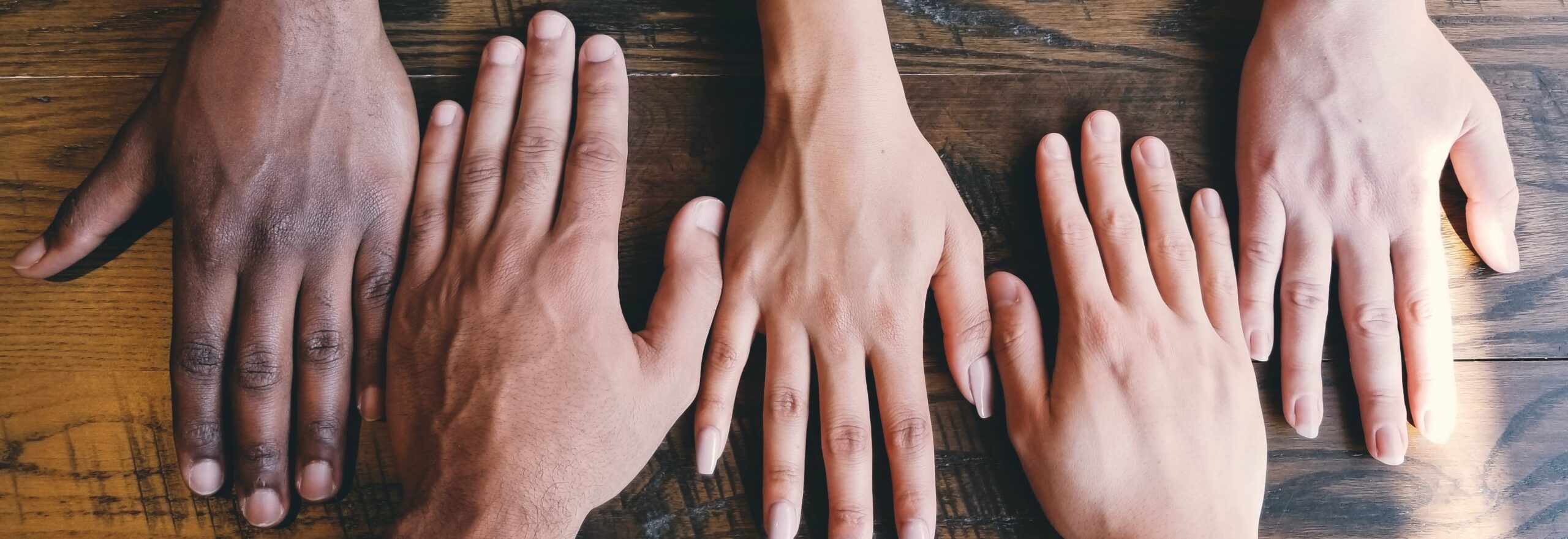 Hands of various skin tones, palm down, in a row on a table. 