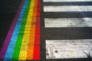 A painted rainbow perpendicular to a white crosswalk.