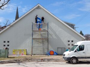 People high on scaffolding, installing first piece of mural on large wall