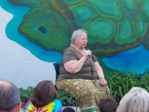 An Elder holding a microphone, in front of the turtle in the mural