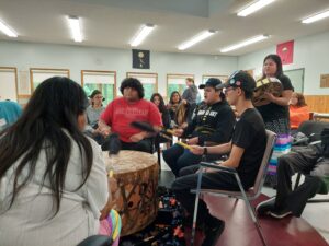 People gathered around a large drum, drumming and singing