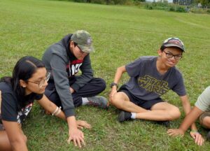 3 youth sitting in a grassy field, playing a game