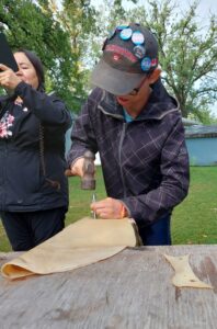 youth working with a hammer and punch to make holes in hide for tying drum 