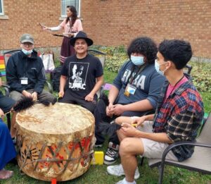 Youth singing and playing around a big Indigenous drum