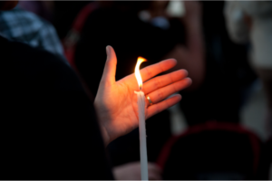 A lit taper candle shielded by an open hand.