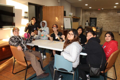 Medium size group sat around a table learning how to use chopsticks