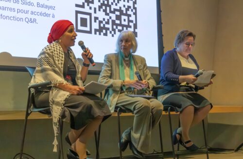 Three women speaking, sitting on chairs in front of a screen. 
