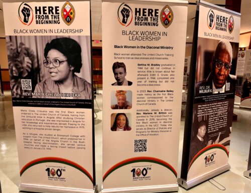 A series of stand up panels featuring a large image of Black individuals on a white background, with text beneath, in a large room.